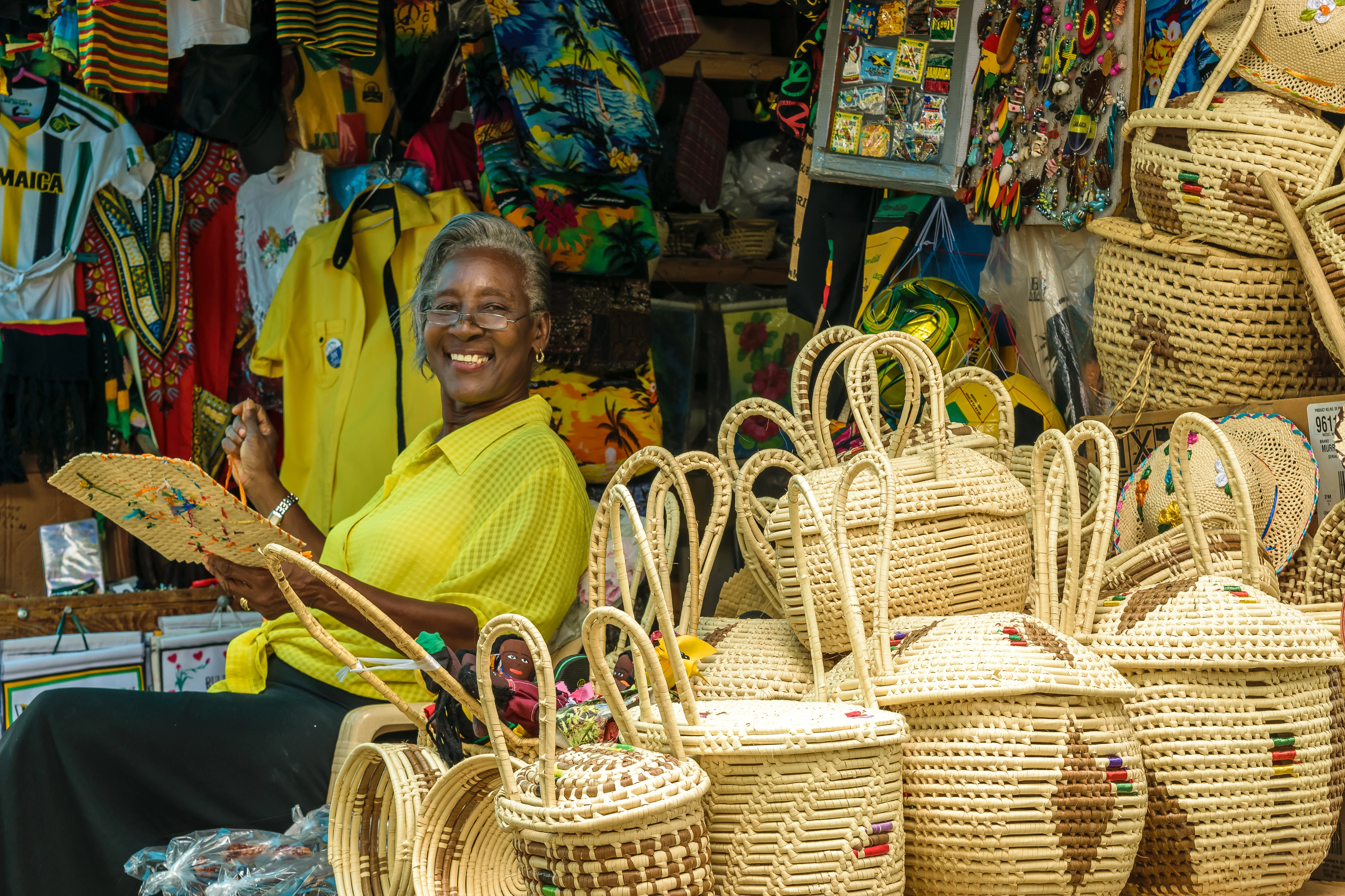 Smiling Jamaican female vendor sitting in her stall with woven baskets and other products at a local craft market in Montego Bay, Jamaica.